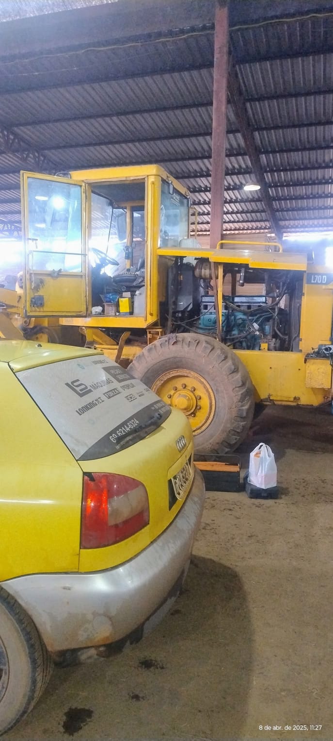 Carro amarelo e pá-carregadeira amarela L70D estacionados dentro de um galpão com teto de telhas metálicas