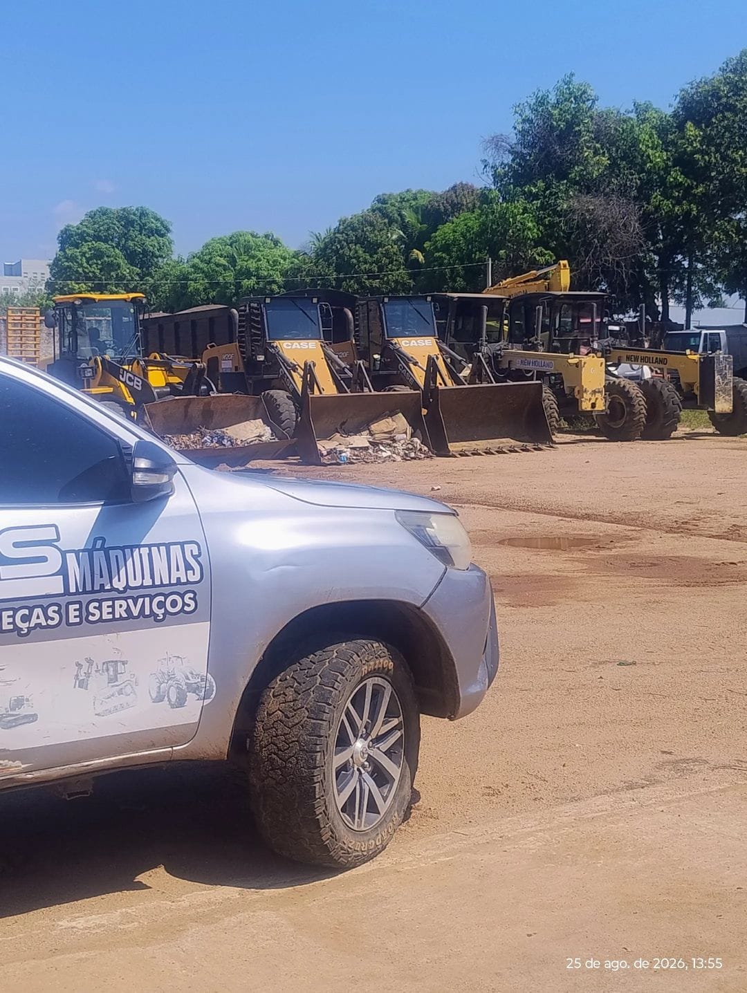 pátio de máquinas pesadas (retroescavadeiras JCB, CASE e New Holland) com um carro prata da empresa em primeir